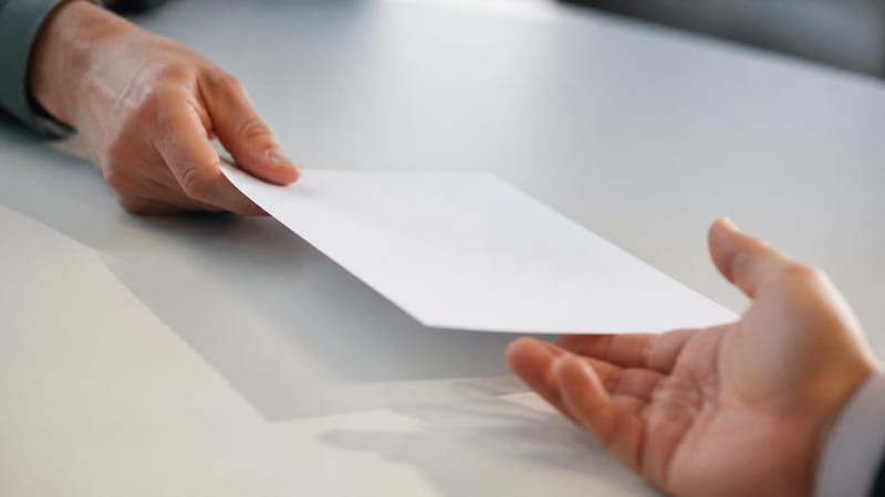 One hand sliding a blank sheet of paper across a pale desk toward another waiting hand